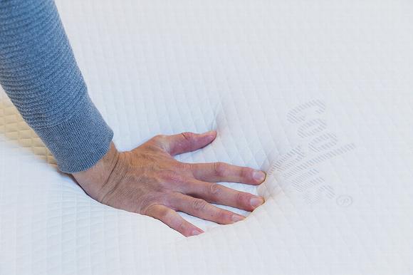 mans hand pushing down on memory foam mattress